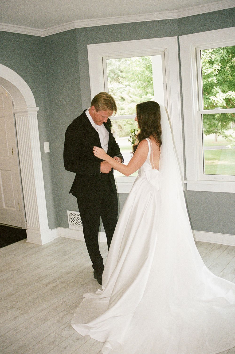 Bride and groom share a tender first look moment indoors, bride in elegant white gown with veil, groom in black suit.