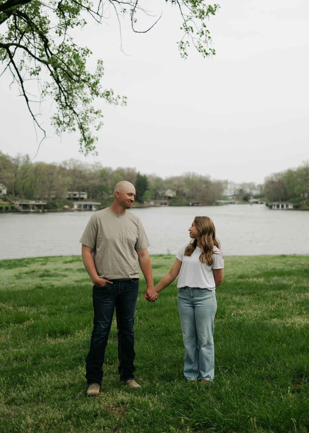 Couple holding hands while standing on green grass near a lake during their engagement photo shoot.