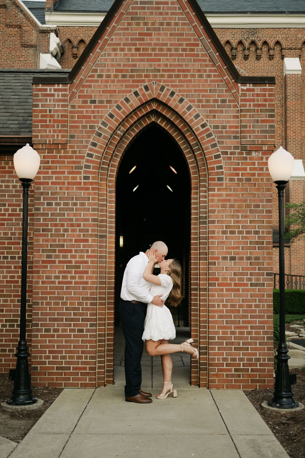 Couple sharing a romantic kiss in the arched doorway of a historic red brick church during engagement session.