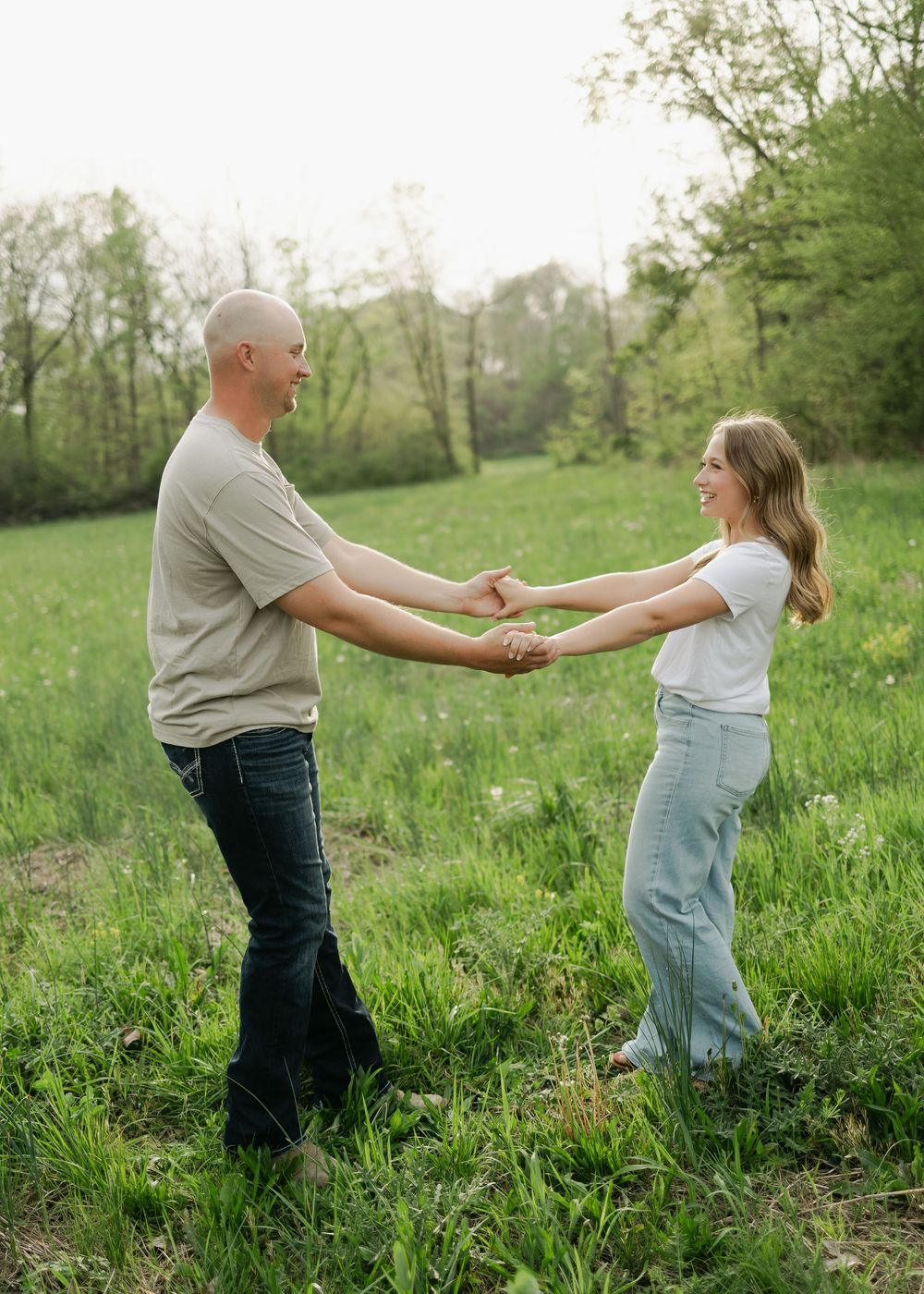 Joyful couple holding both hands and smiling while dancing together in a beautiful green field at sunset.