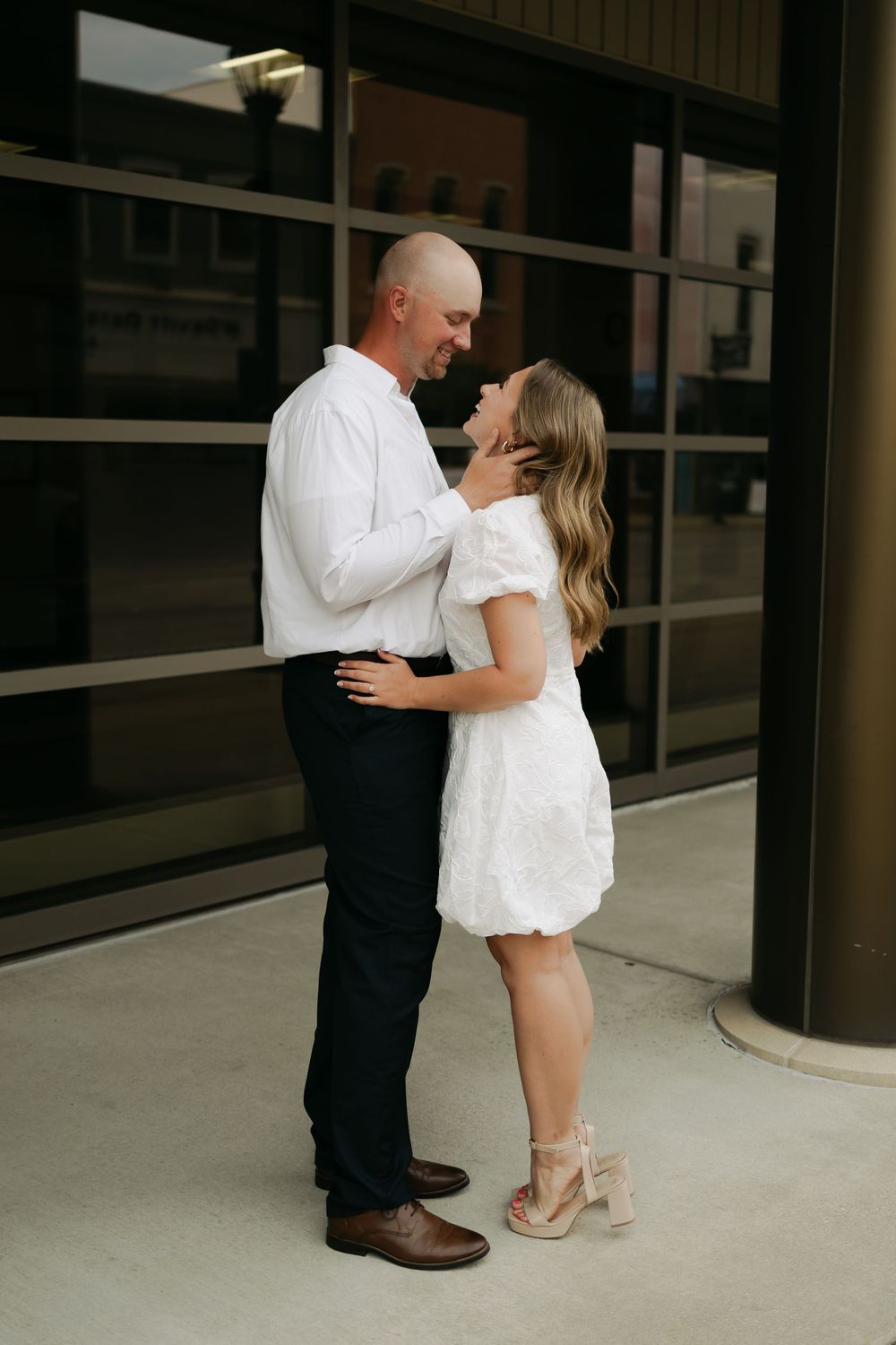Couple in coordinating white outfits share a romantic embrace outside a modern building.