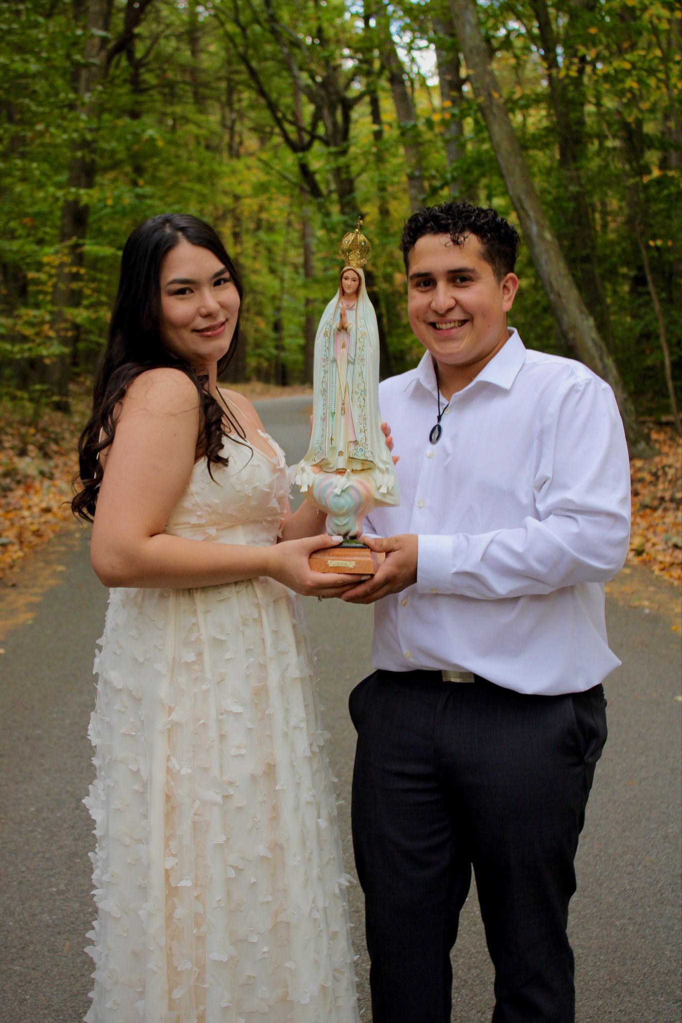 Couple in wedding attire playfully shares cake in autumn woodland setting.
