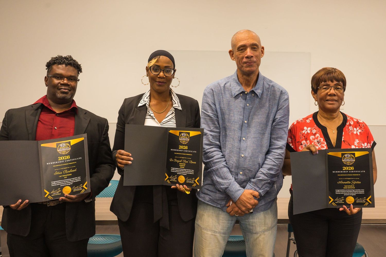 Four people posing together holding black award certificates at an academic ceremony.