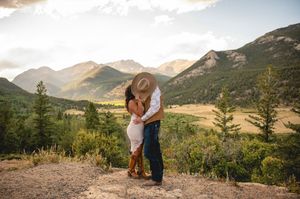 Couple kissing on a rocky overlook with stunning mountain valley views and golden sunset light in Colorado.