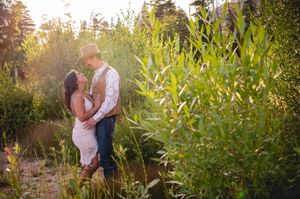 Couple sharing a romantic moment surrounded by lush green foliage in golden hour sunlight outdoors.