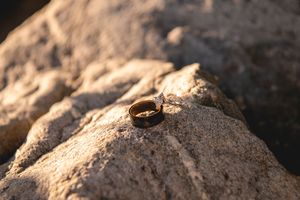 A gold wedding band resting on a textured rocky surface in warm golden sunlight.