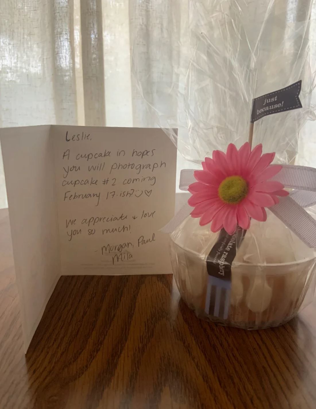 A handwritten thank you note displayed next to a pink gerbera daisy flower in a glass container.