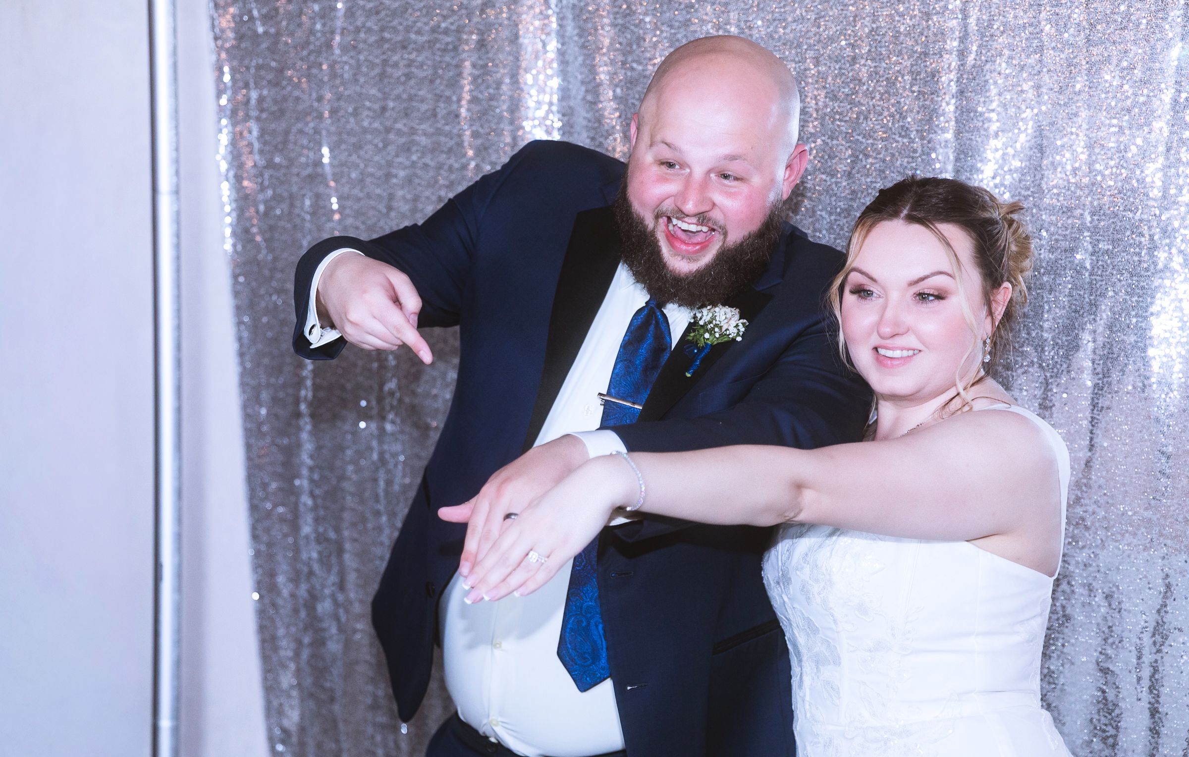 Happy bride and groom posing playfully in front of a silver sequin backdrop at wedding photo booth.