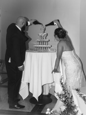 Bride and groom pouring champagne tower at wedding reception in elegant black and white photo.