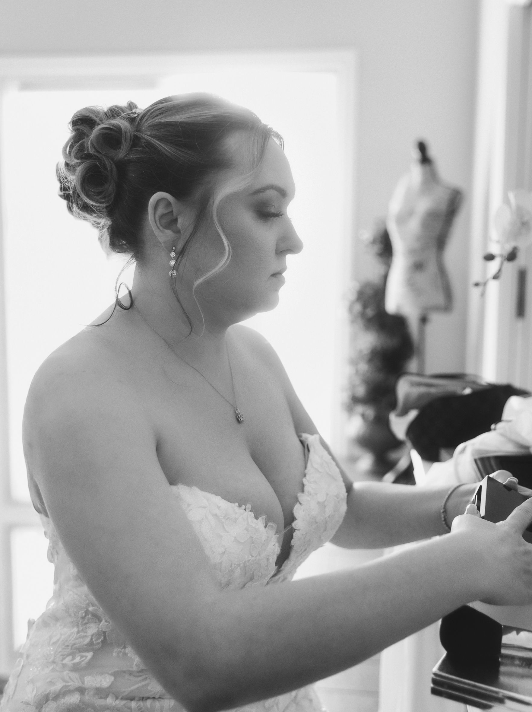 Bride in strapless lace gown with updo hairstyle preparing on wedding day in black and white.