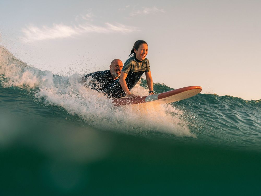 water POV photo of a son and father laughing and taking off on a wave at sunset Bar Beach, Newcastle NSW