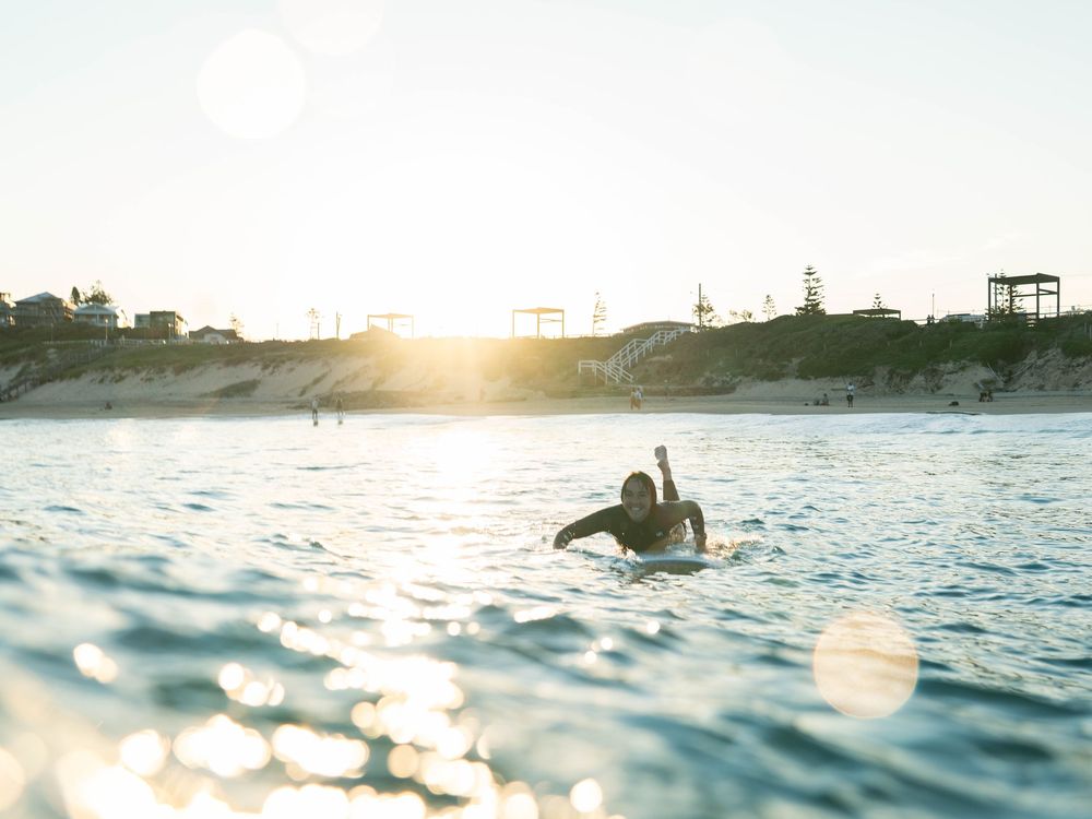 photo of a girl paddling back to the lineup with a smile on her face at sunset Bar Beach, Newcastle NSW