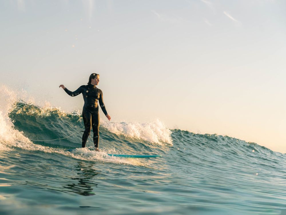 photo of a woman surfing at Bar Beach, Newcastle at sunset with blue wave lines and golden light in spring