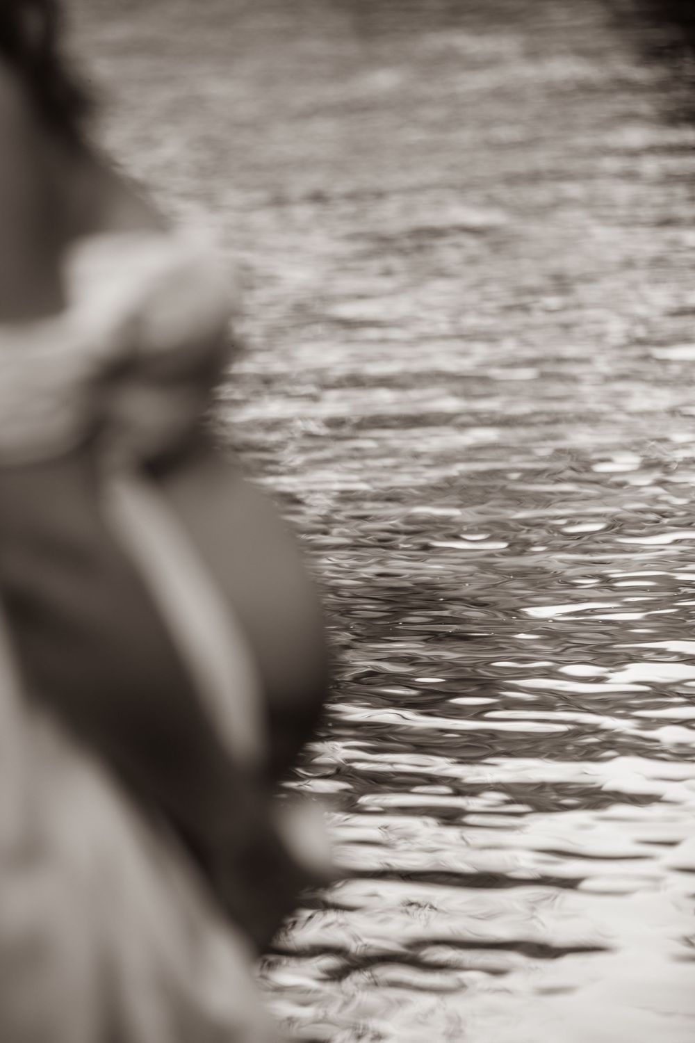 Black and white abstract image of pregnant woman's silhouette beside rippling water surface Cornwall Maternity Photographer