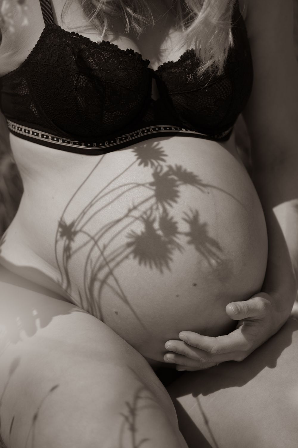 Black and white close-up of pregnant woman's bare belly with floral shadows cast across her bump Cornwall Maternity Studio
