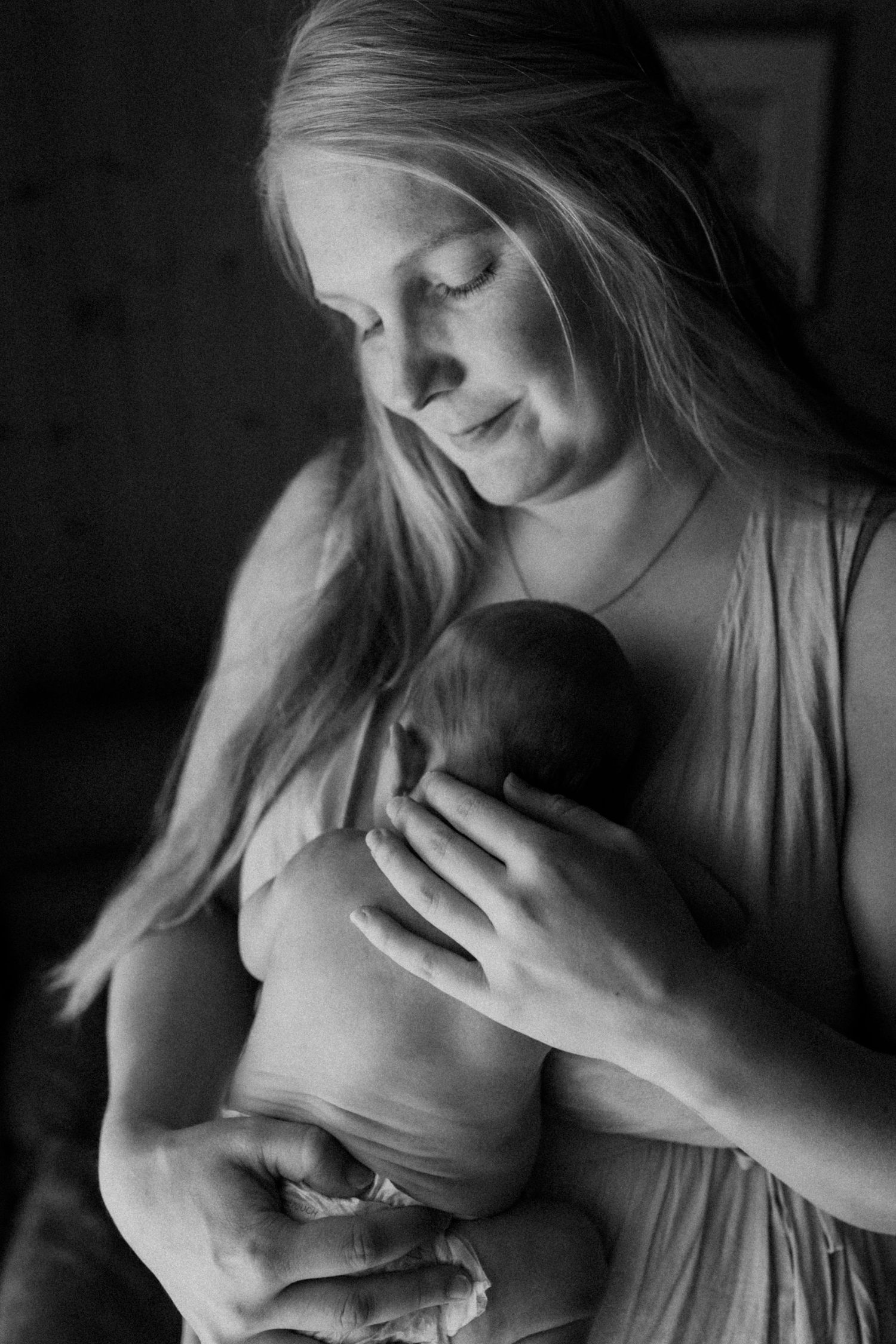 Vastasyntynyt vauva vaippasiltaan äidin sylissä perheen kotona postpartum-kuvauksessa. Äidin käsi silittää hellästi vauvan selkää.
