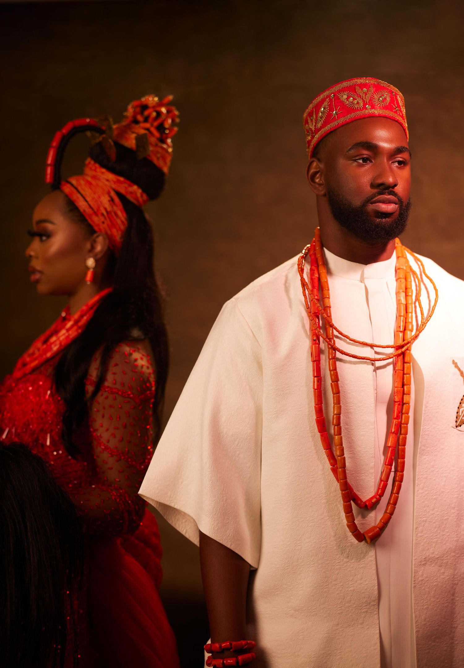 Man and woman in traditional Nigerian attire with red coral beads and headpieces at a cultural ceremony.