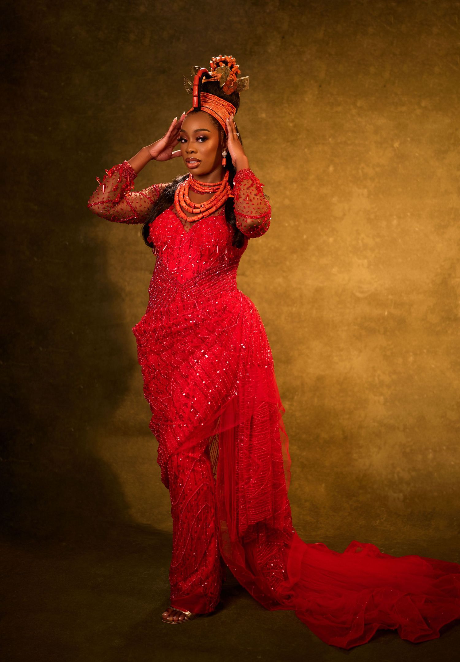 Woman in stunning red Nigerian traditional bridal gown with coral beads and ornate headdress.