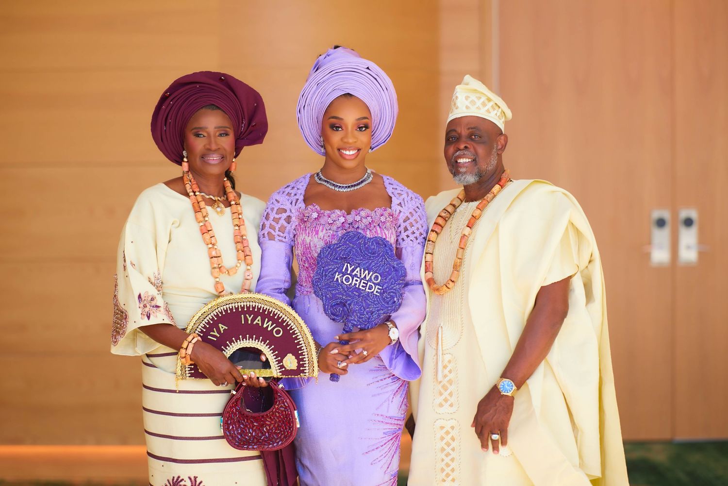 Three people in vibrant traditional Nigerian attire pose together at a formal celebration event.