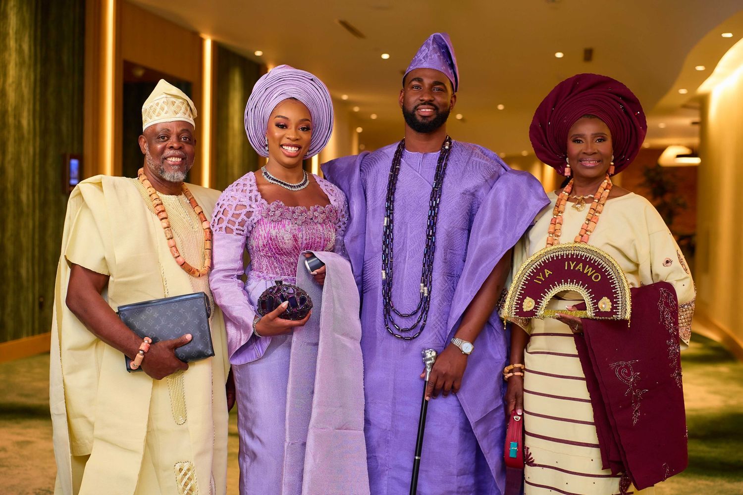 Four people in vibrant traditional Nigerian attire smile together at a formal celebration event.