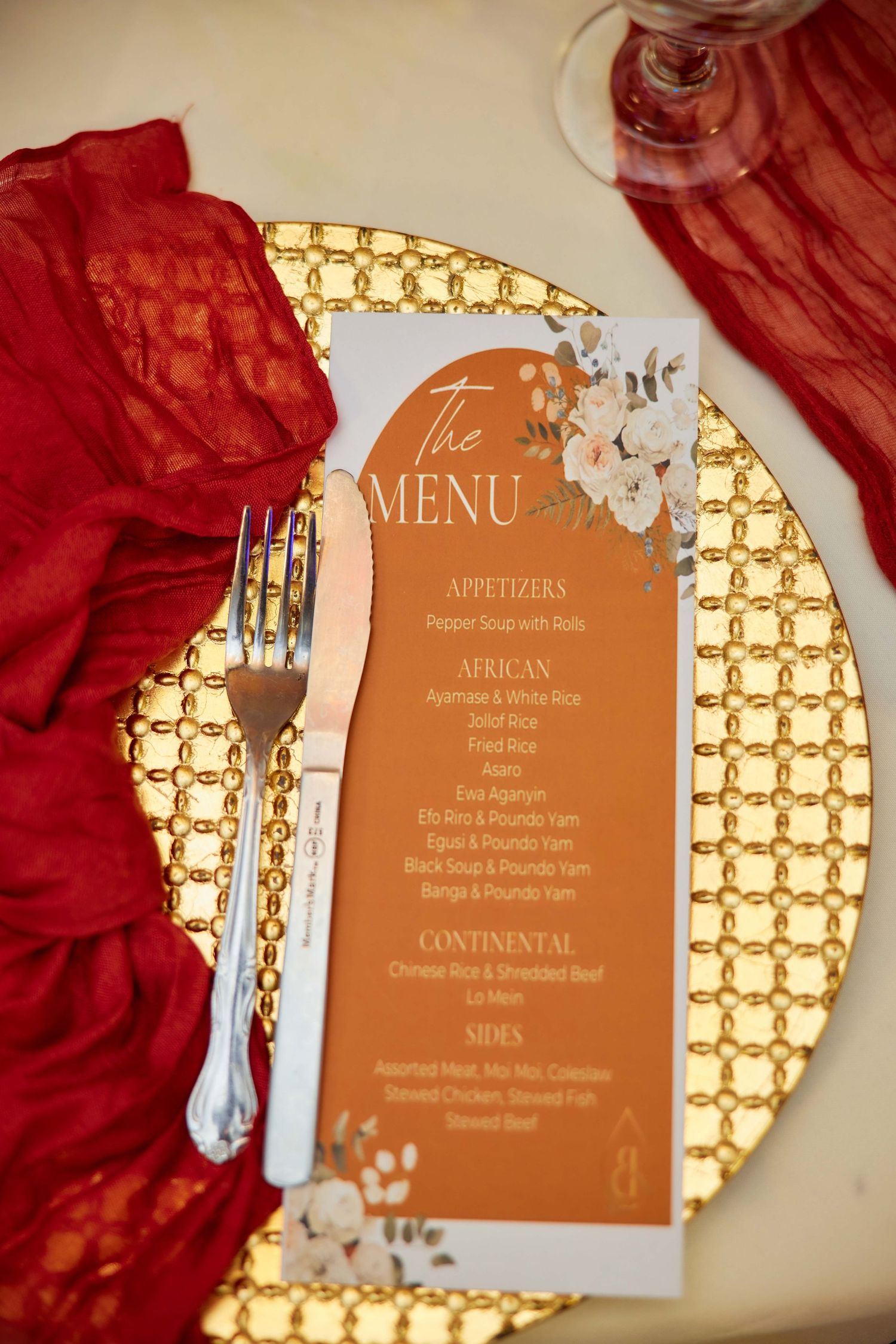 Elegant wedding menu card on gold charger plate with red lace napkin, fork, and floral design detailing appetizers and entrees.