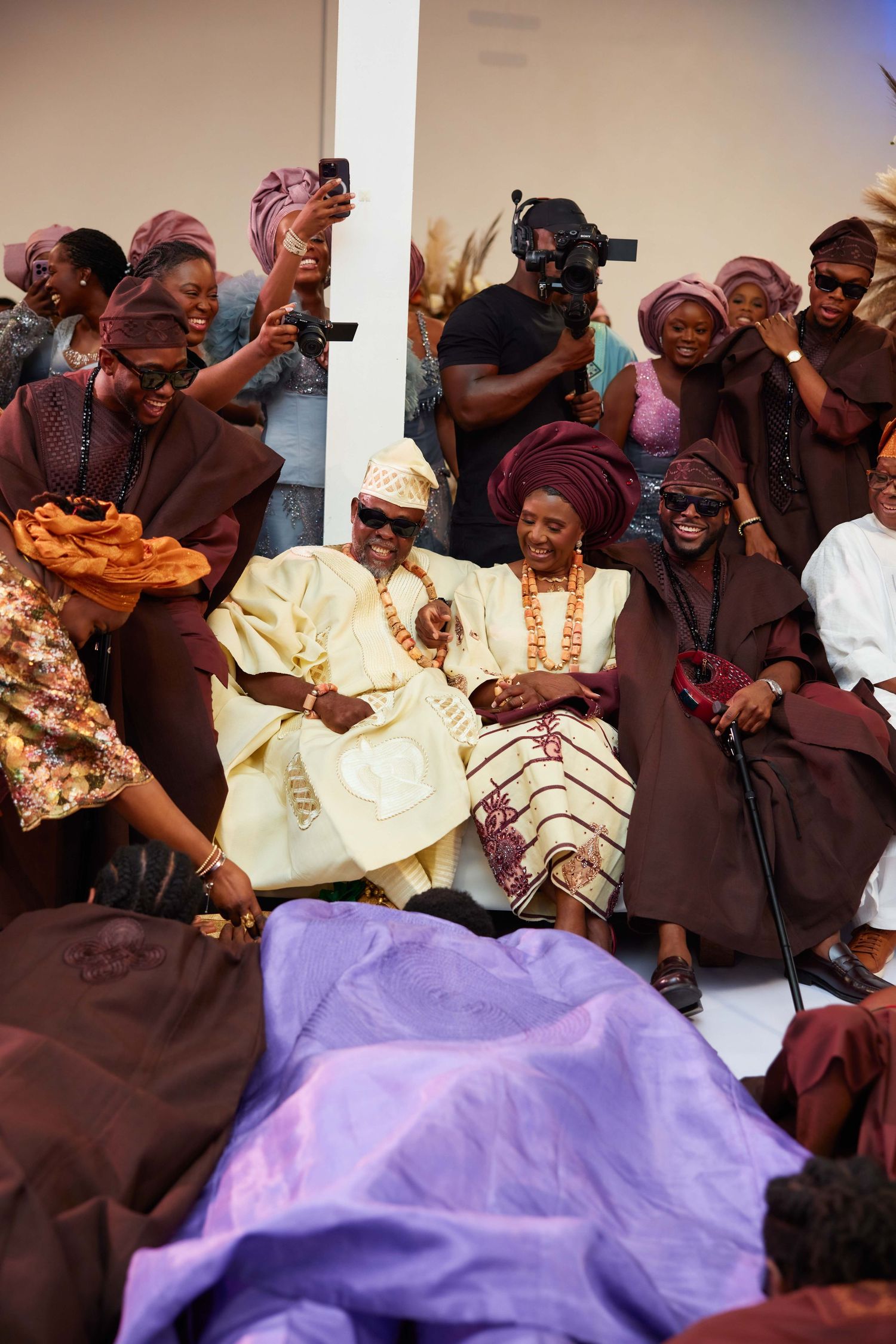 Joyful West African traditional wedding ceremony with guests in matching burgundy attire celebrating the couple.