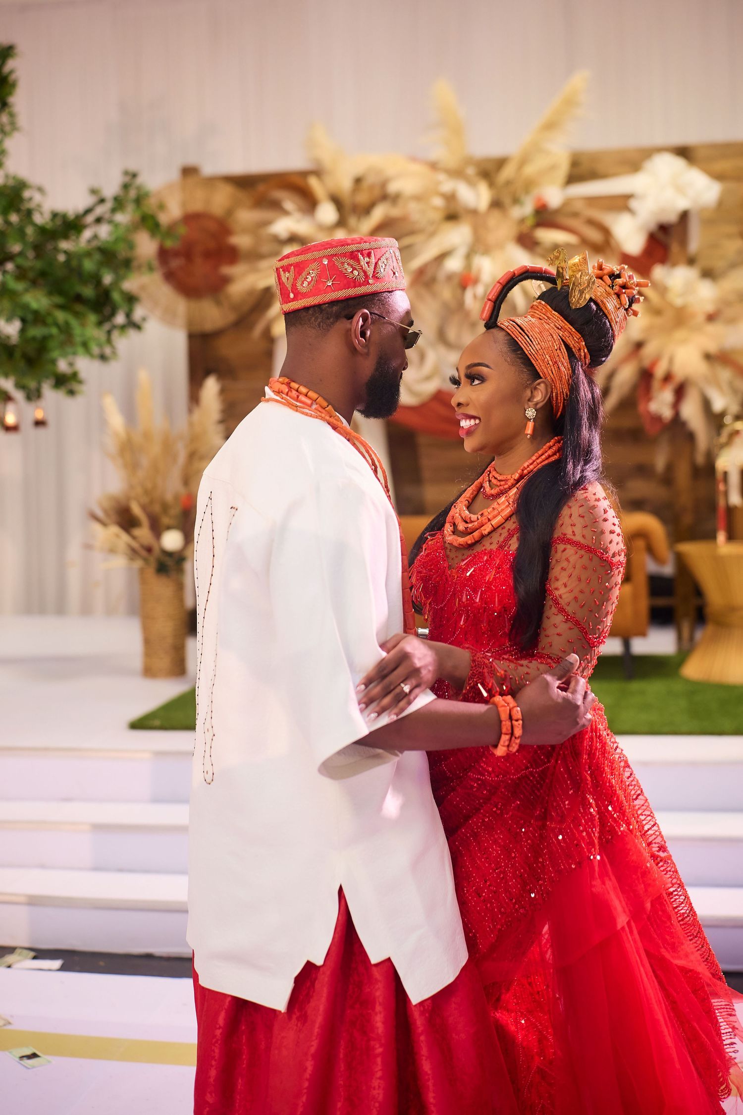 Nigerian couple in traditional red and white wedding attire sharing a romantic moment at a cultural ceremony.