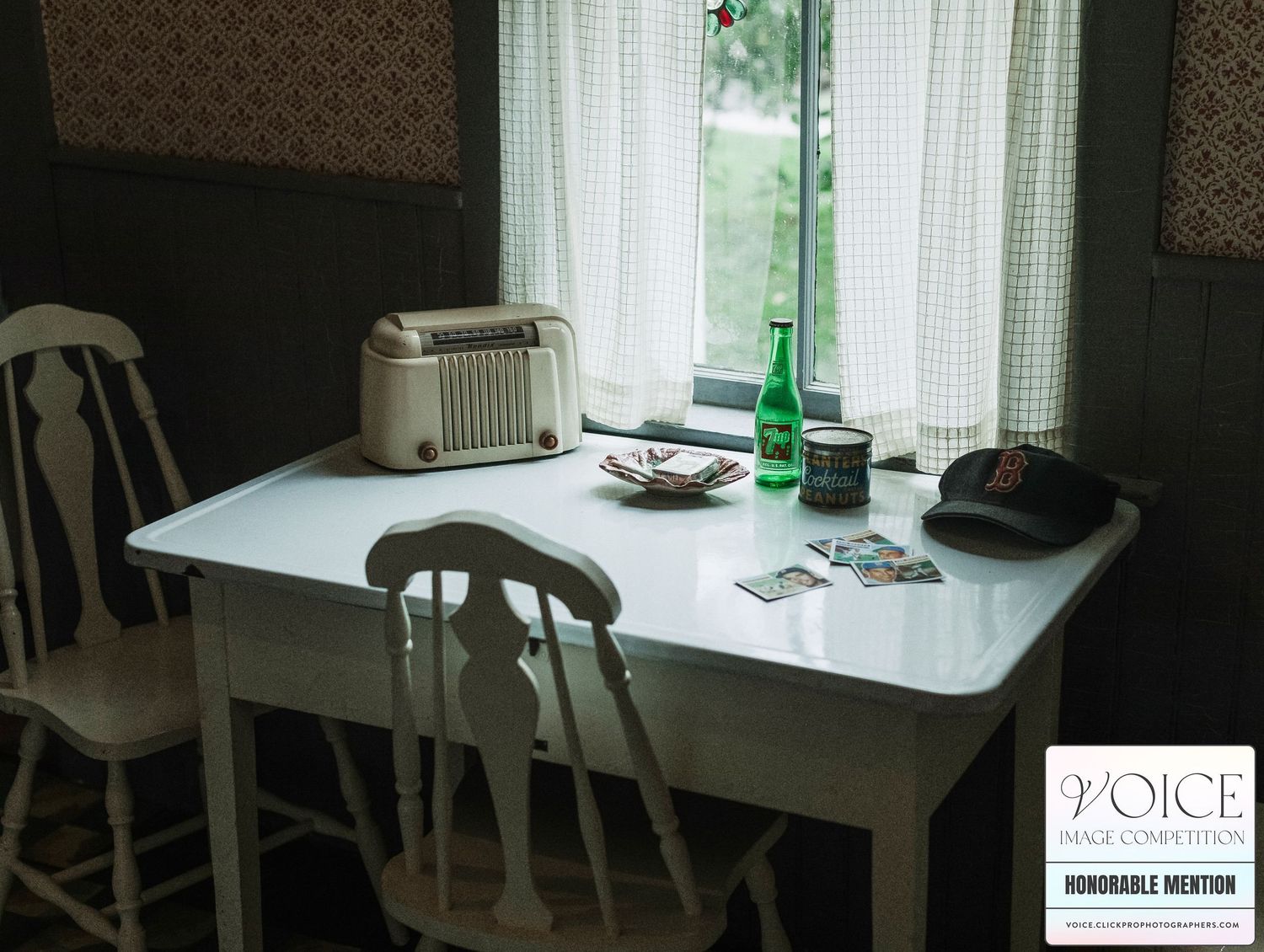 Vintage white kitchen with baseball cards, baseball cap, and glass bottle on metal table with sheer plaid curtains behind. NH photographer