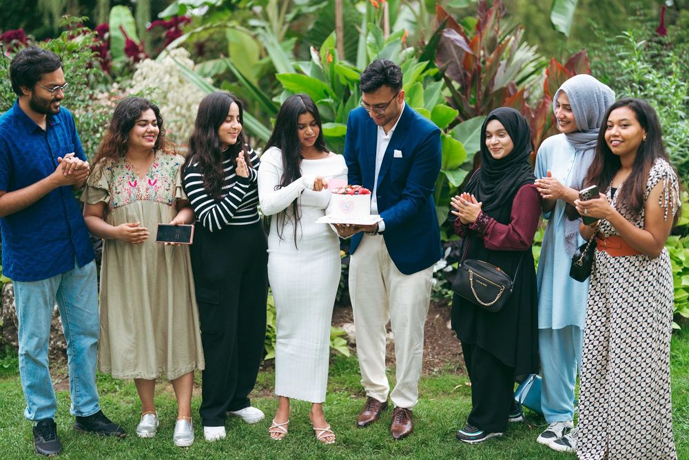 Group of friends celebrating outdoors in a garden, sharing a cake during a joyful gathering.