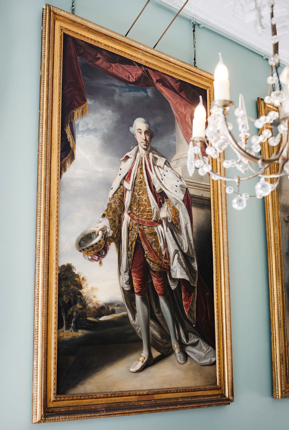 Large ornate gold-framed portrait of an 18th-century nobleman in ceremonial dress on a teal wall.