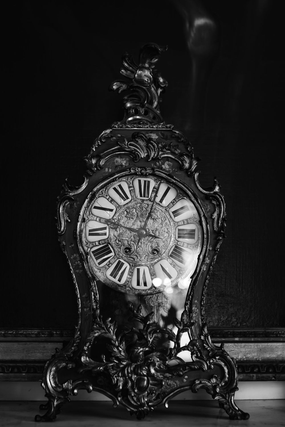 Ornate antique Baroque mantel clock with Roman numerals in dramatic black and white photography.