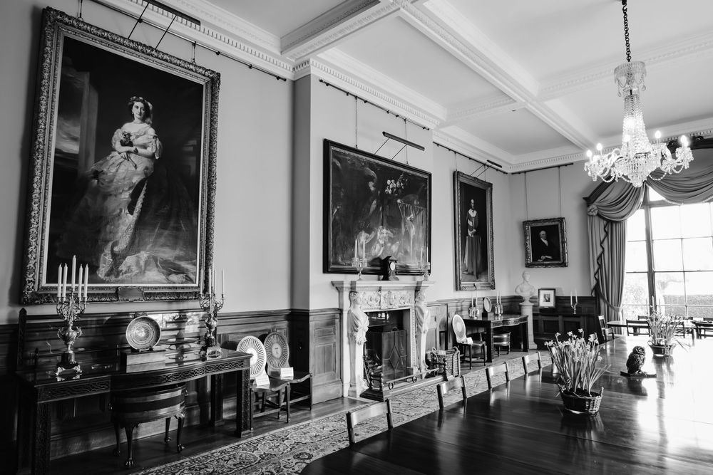 Black and white photo of grand formal dining room with large portraits and crystal chandelier.