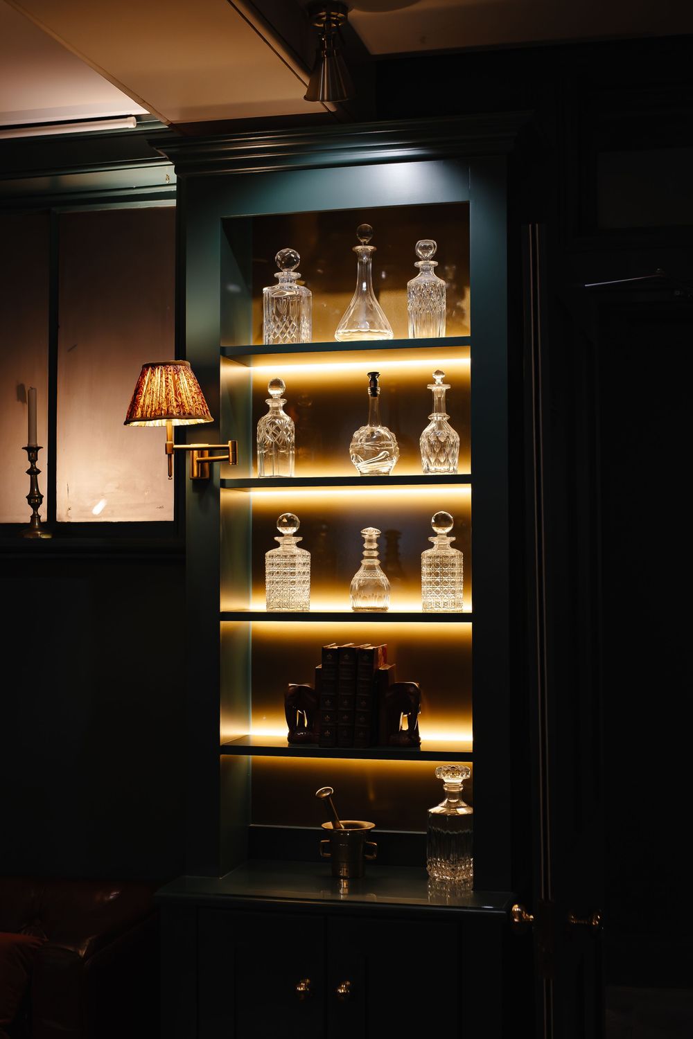 Illuminated display cabinet showcasing crystal decanters on glass shelves in a dark elegant interior.