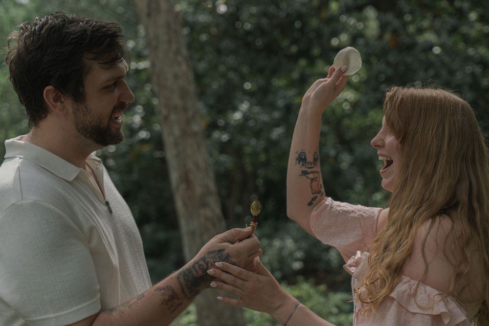 A tattooed couple laughs and plays together in a lush wooded garden during an engagement session.