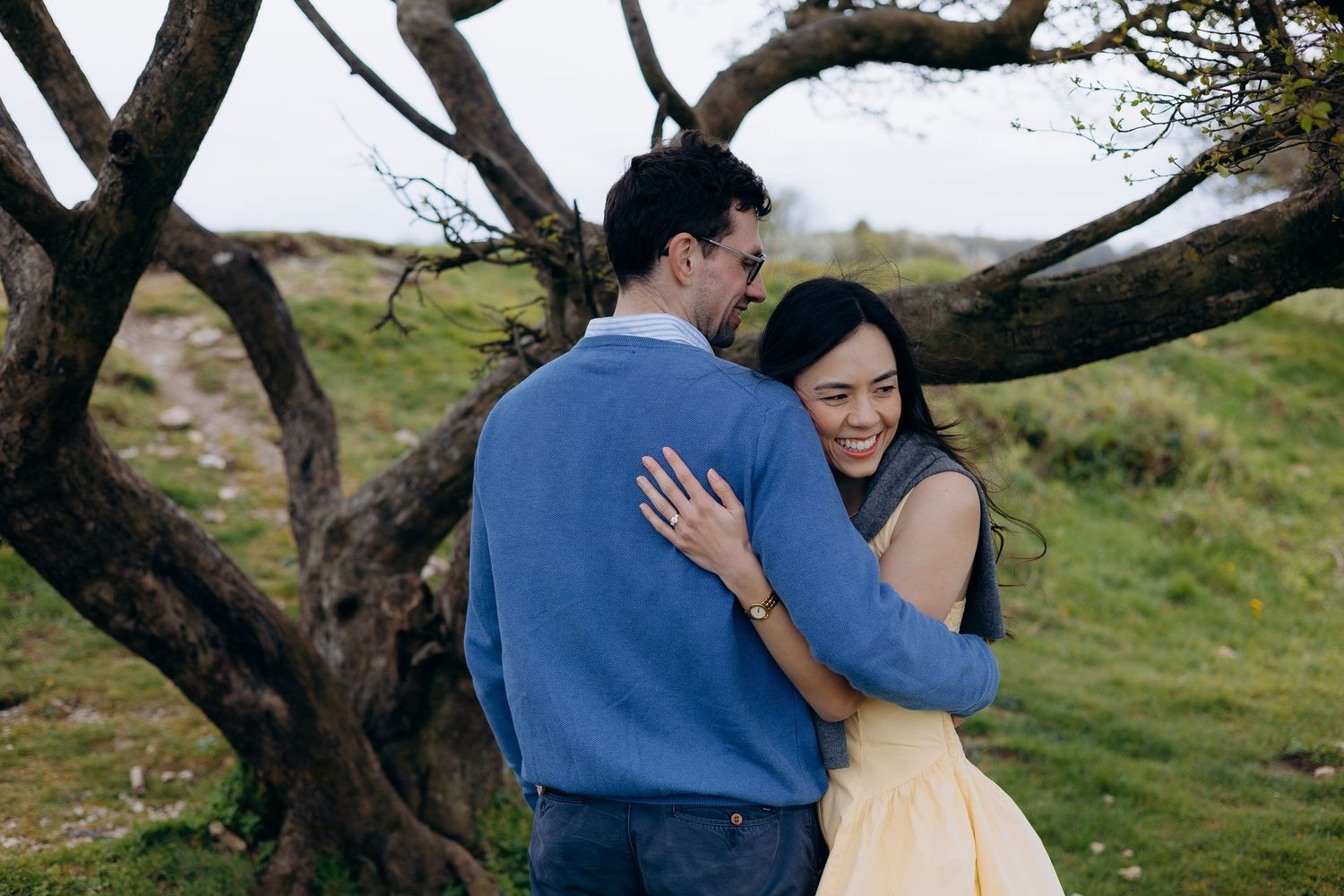 Couple standing on a lush green hillside overlooking a scenic valley and town on a cloudy day.