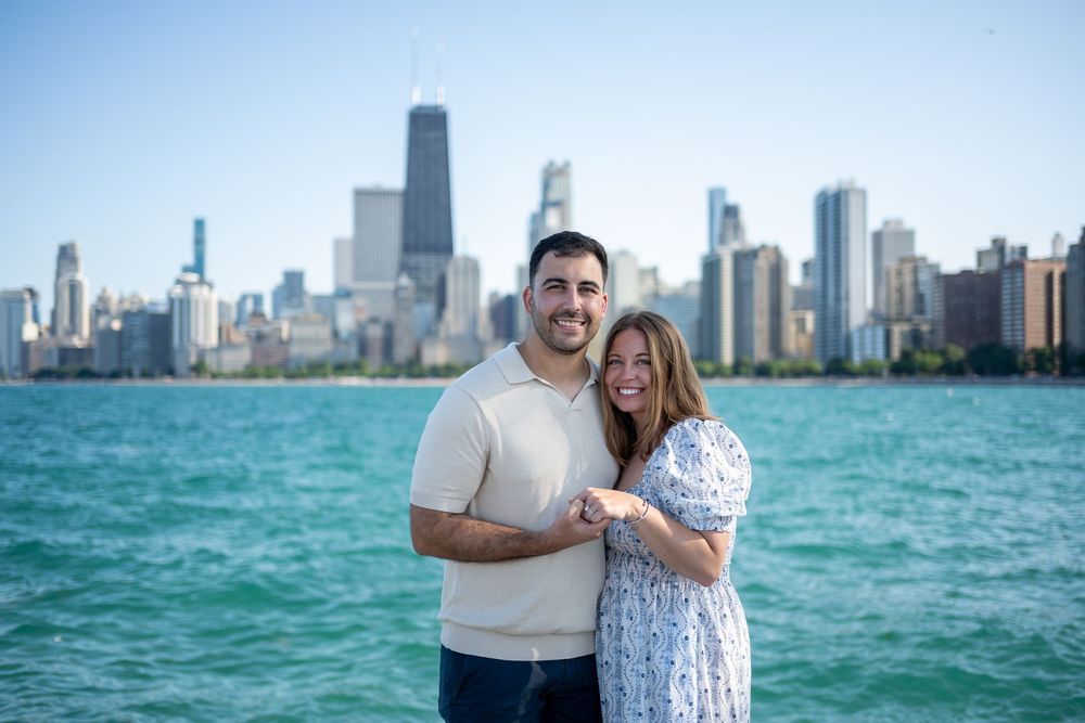 Couple smiling and holding hands in front of Chicago skyline and Lake Michigan on a sunny day.