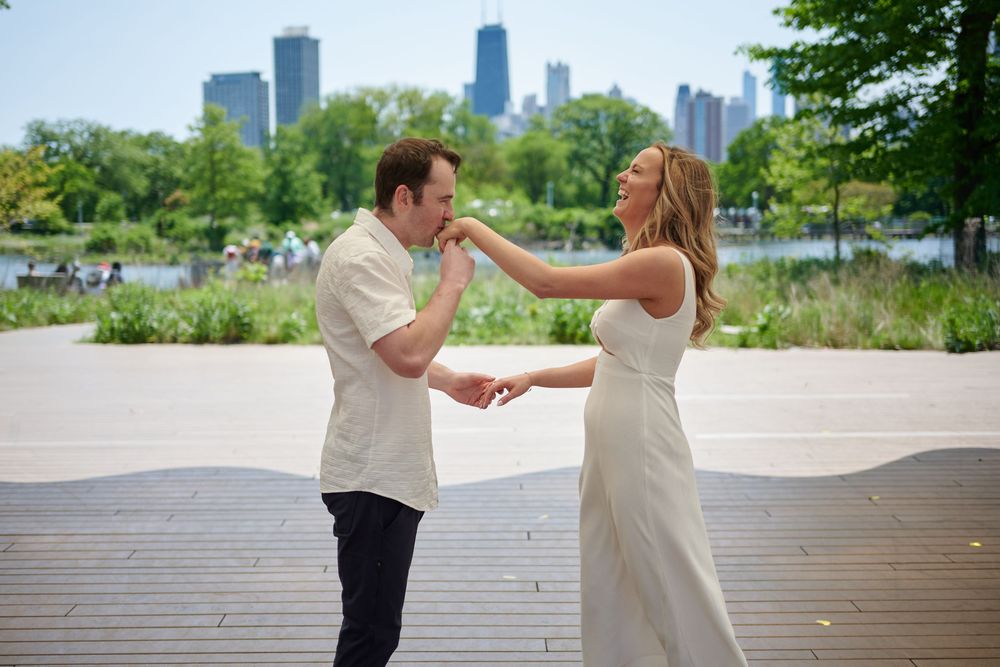 Couple dancing outdoors near Chicago skyline, woman in white dress, man in white shirt, urban park setting.