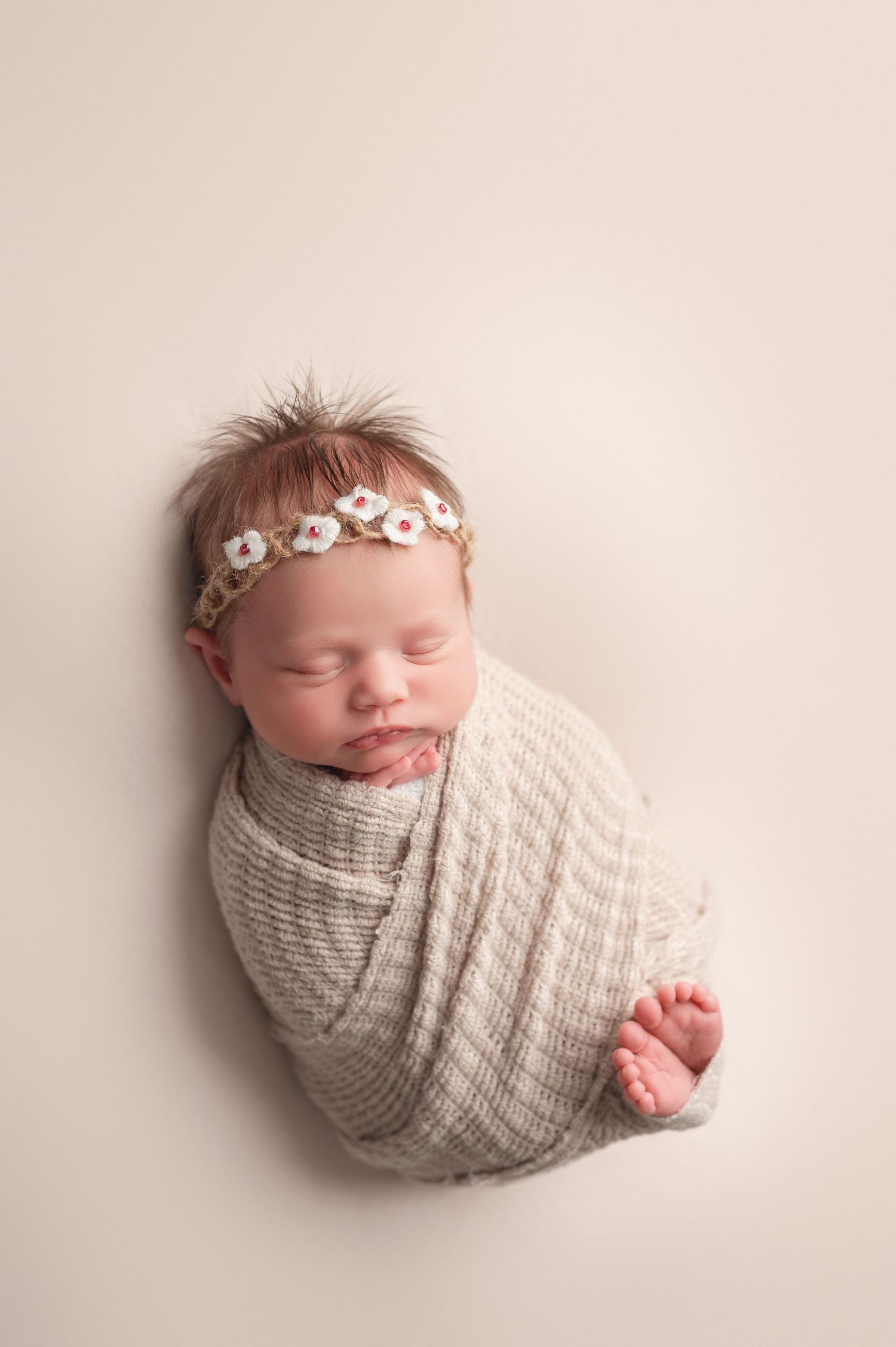 A sleeping newborn wrapped in white fabric lies peacefully in a rustic woven basket on a dark wooden floor.