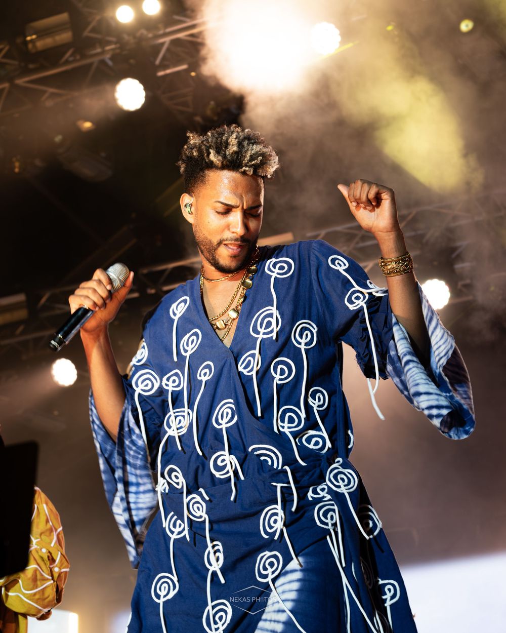 Male artist performing on stage in blue African print robe holding microphone.
