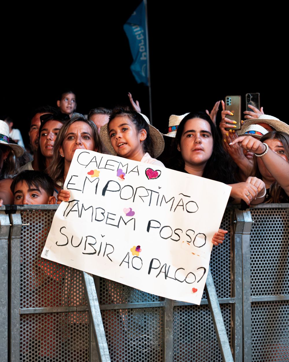 Fans at a concert in Portimão holding a sign in Portuguese asking to join the artist on stage.