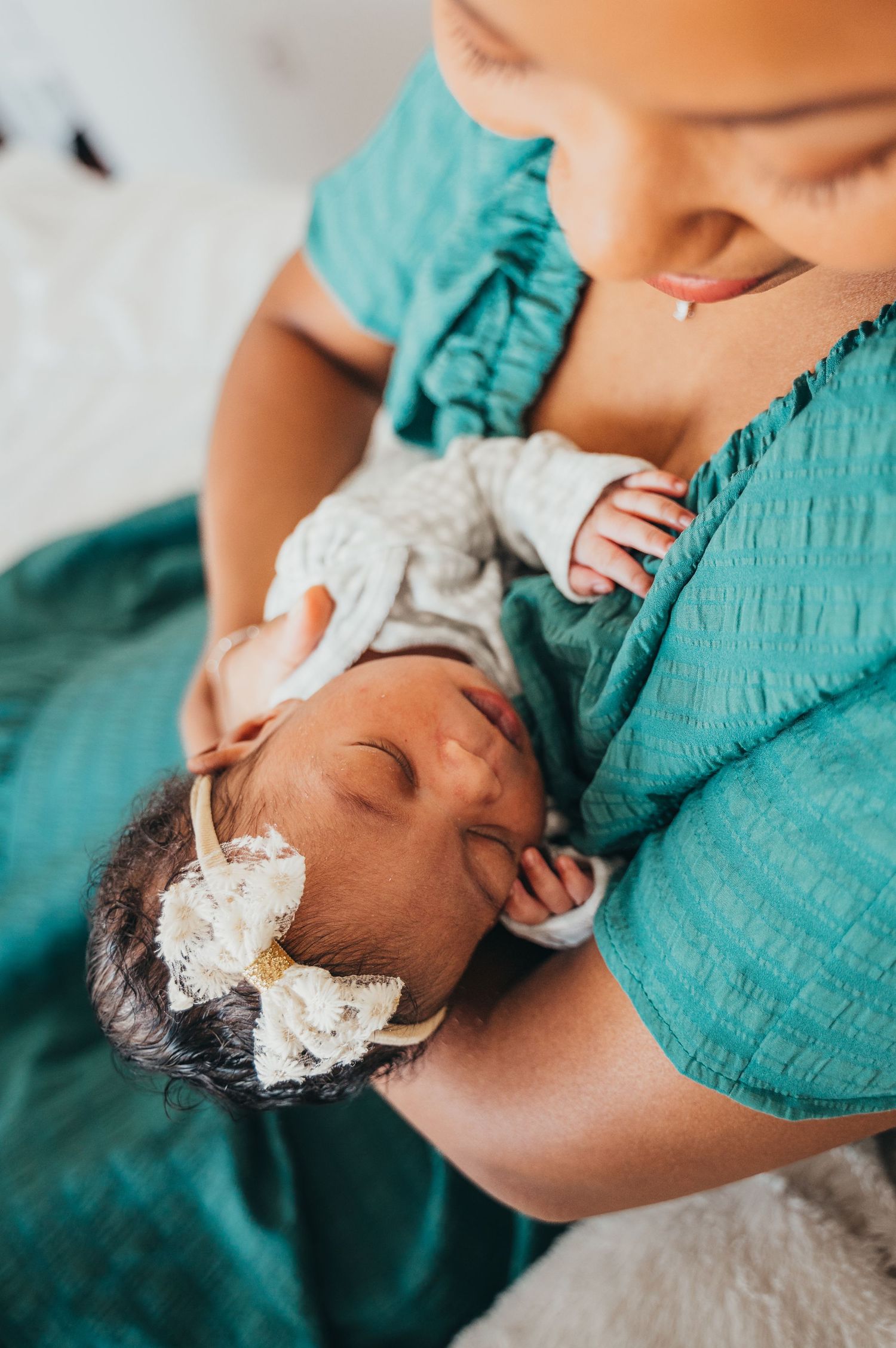 Mississauga newborn photographer captures mom sitting on white bed holding newborn baby while she sleeps.