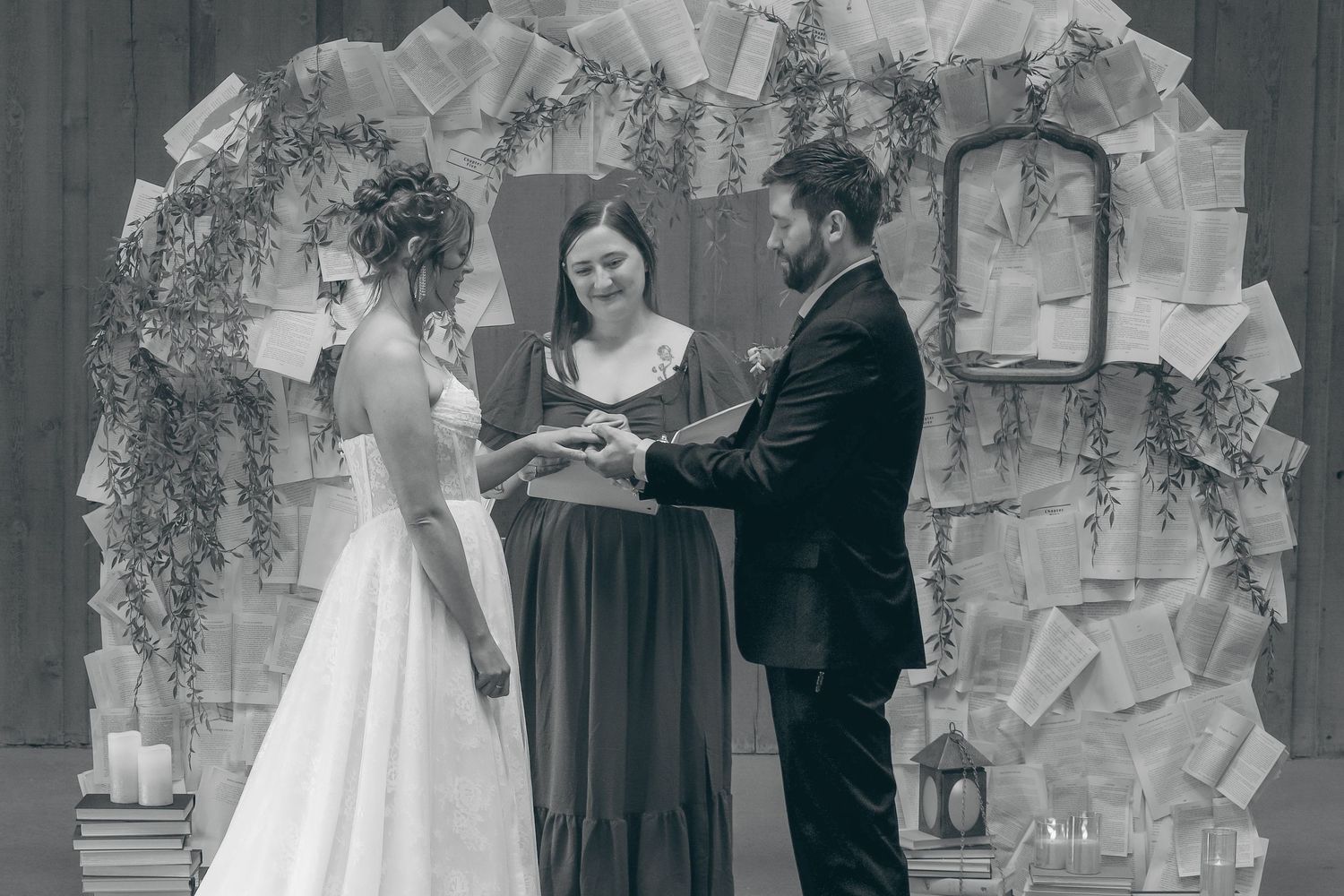Black and white wedding ceremony photo with bride, groom, and officiant standing under a decorative arch.