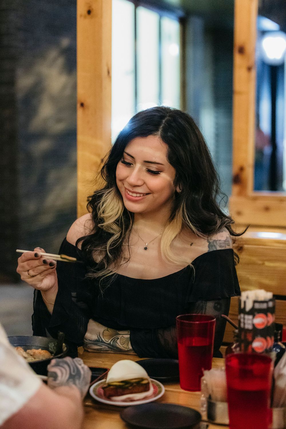 Smiling woman with tattoos holding chopsticks at a restaurant table at Fulton Market in Chicago during engagement session