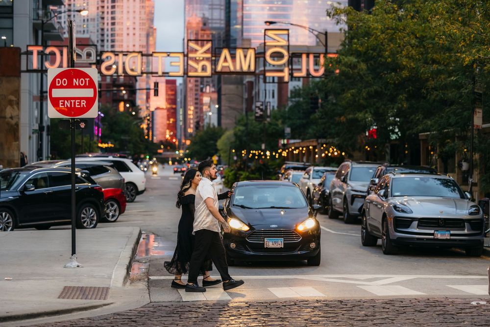 Couple crossing a busy urban street at dusk with city lights at Fulton Market in Chicago during engagement session