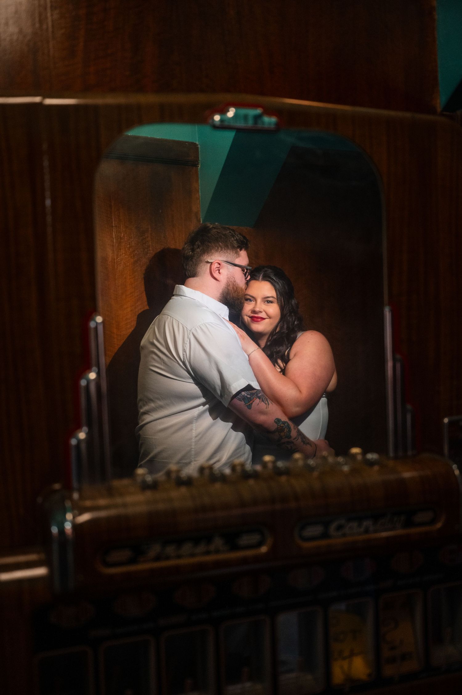 Couple sharing a romantic embrace near a vintage jukebox in a dimly lit bar setting.