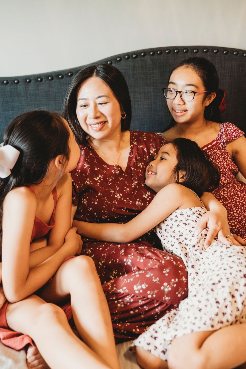 Mom cuddles with her three daughters while smiling and cuddling with them on her bed.