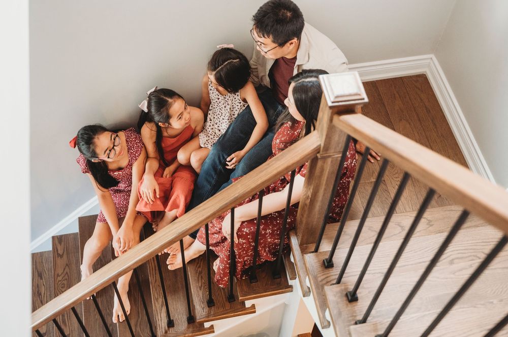 A Mom and Dad and three daughters sit closely on the stairs talking and playing while Mississauga photographer captures it from above.