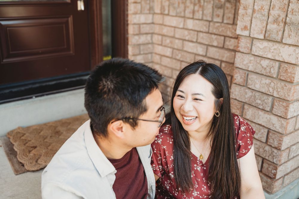 A woman looks at her husband smiling and laughing while they sit on their front porch