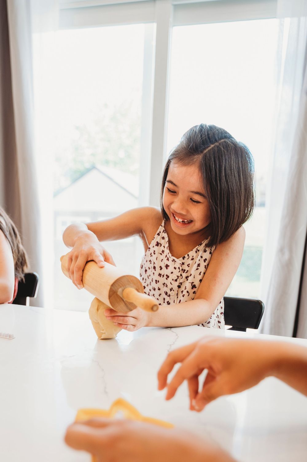A little girl holds a rolling pin and tries to roll out some dough on her kitchen counter.