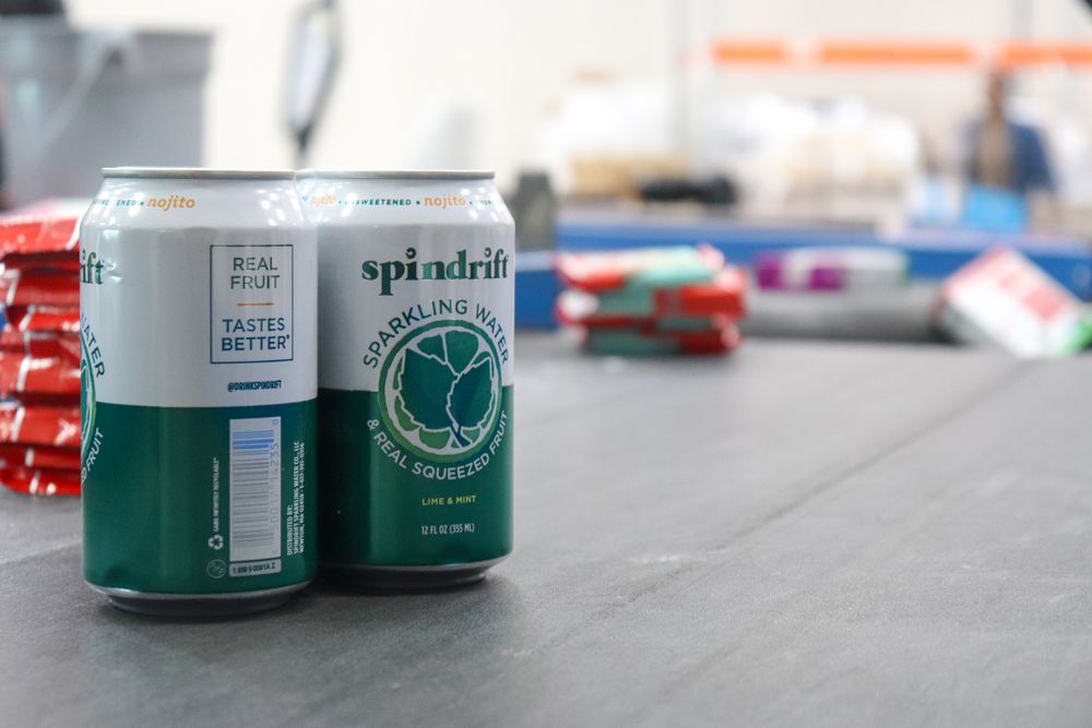 Two green Spindrift sparkling water cans on a gray surface in a warehouse setting.